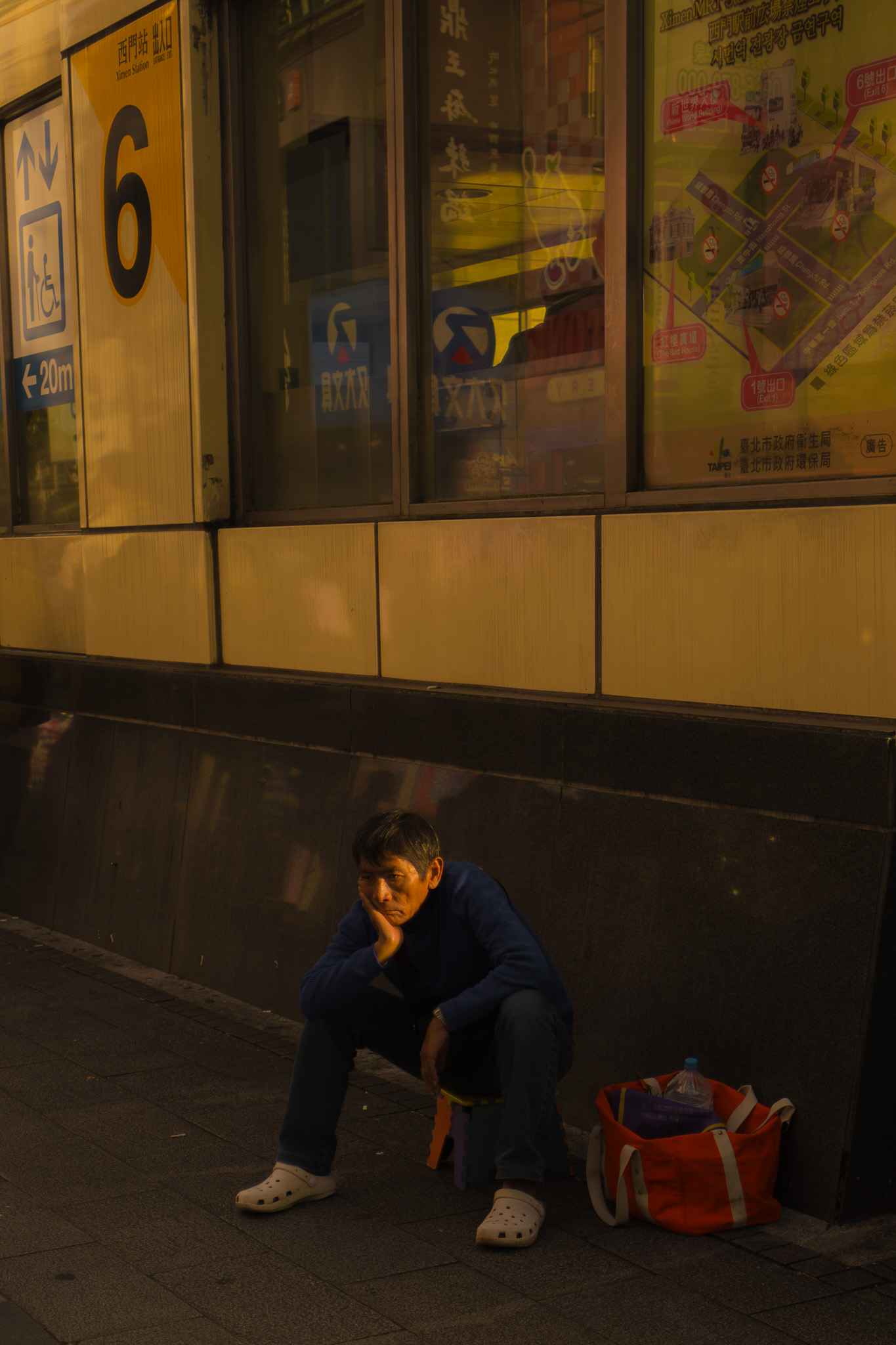 Man sitting on a stool below transit signs at night